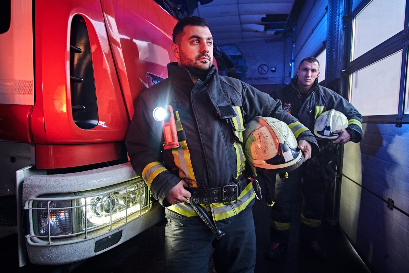 two firemen standing near the fire truck at night in a fire depot